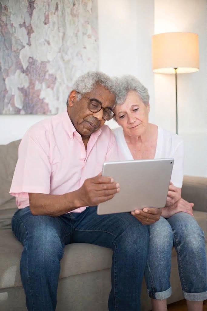 An older couple sitting together on a sofa, looking at a tablet